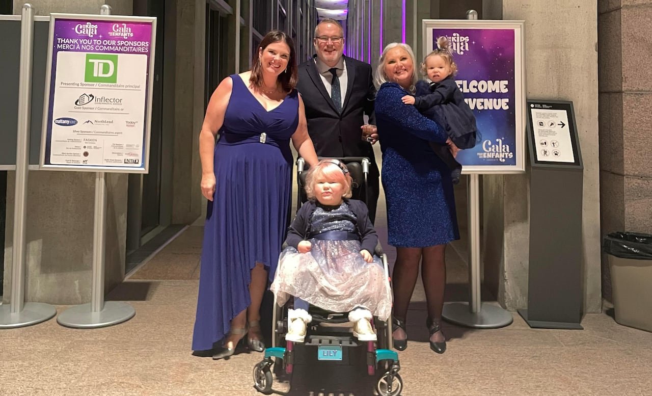 A group of smiling people pose for the camera together. The two women and girls are wearing blue dresses and the man is dressed in a blue suit.