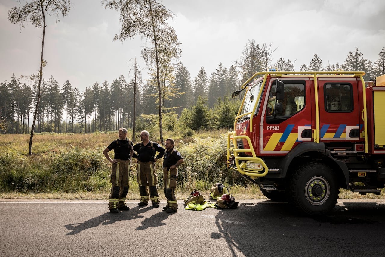 default-10 Three firefighters stand near an emergency car near a wildfire.